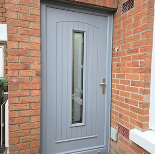 Grey door with vertical glass panel, brick walls, and silver handle WarmHaus Windows & Doors