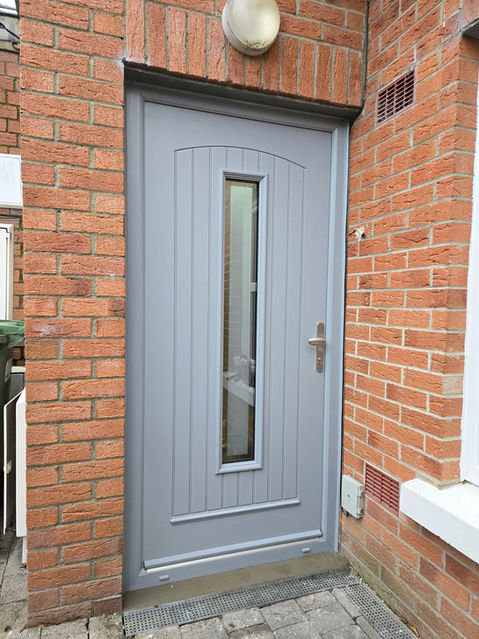 Grey front door with glass panel and brick surround, WarmHaus Windows & Doors.