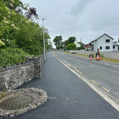 Newly paved road and sidewalk, stone wall on left