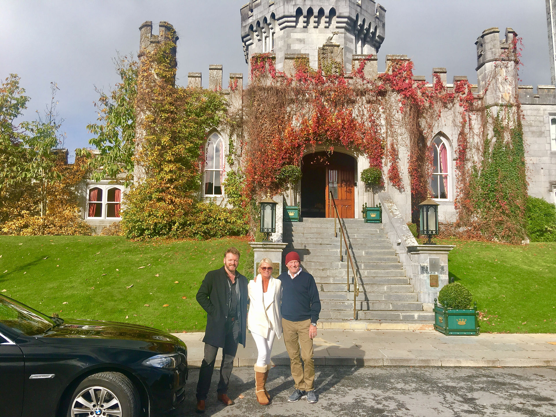 Three people posing outside Dromoland Castle with a car; Ireland Tours.