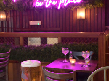 Neon sign says "This must be the place" above table and drinks.