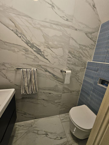 Modern bathroom with white marble tile, toilet, sink, and towel rack setting.