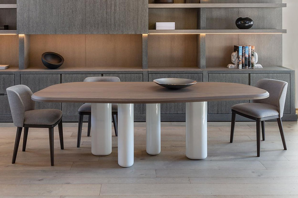 Ovale eettafel met houten blad en drie cilindervormige poten in glanzend wit, geplaatst in een moderne eetruimte met open houten kast en neutrale tinten. De combinatie van materialen benadrukt de sculpturale eenvoud van het ontwerp.