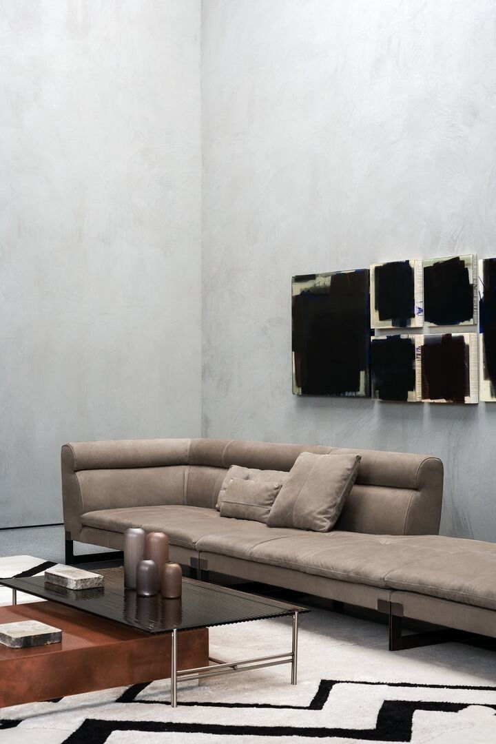 Moderne woonkamer met een hoekbank bekleed met Kashmir Souris leer van Baxter, strak en minimalistisch design, met een geometrisch vloerkleed en betonnen muur op de achtergrond. Ideaal voor een blogpost over het kiezen van leer, waarbij de luxe en kwaliteit van Baxter lederen meubels worden benadrukt.