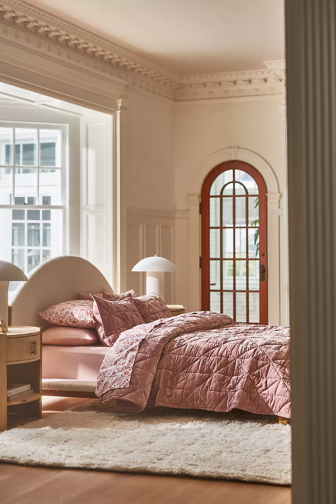 Elegant ingerichte slaapkamer met groot bed en Peach Fuzz gekleurd beddengoed, witte nachtkastjes, en grote ramen met uitzicht op herfstbomen