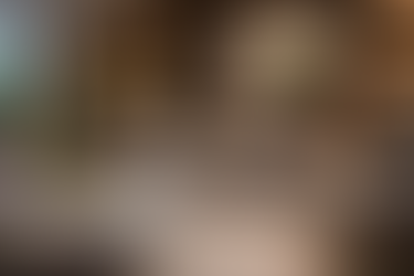 Showroomopstelling met een ronde taupekleurige bank, lage witte salontafel en wandkast van donker hout met geïntegreerde verlichting en abstract schilderij erboven.