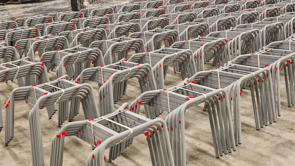 Rows of stacked grey Spaceforme en classic metal chair frames, bound by white straps, on a warehouse floor.