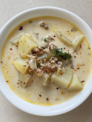 looking down into a while bowl filled with creamy white zuppa toscana soup with pops of green kale and crushed red pepper flakes on top as a garnish