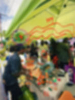 melon nation community members gather beneath a green market tent while fresh seeded watermelon is sliced & shared during a black-led cultural wellness marketplace activation. the scene features handcrafted melon products, community exchange, food sovereignty, & vibrant artistic overlays reflecting creativity, collective care, & agricultural storytelling.