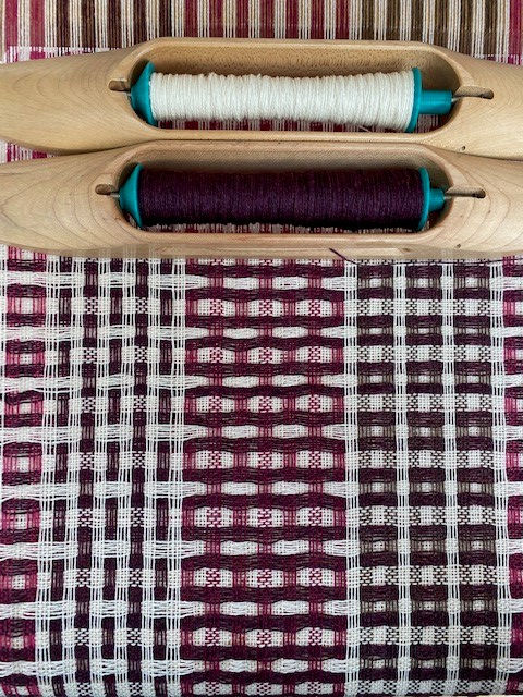 Thumbnail: weaving on the floor loom of a burgundy pink and white patterned and textured handwoven scarf fabric
