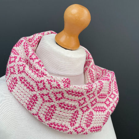 White mannequin with pink patterned scarf against a dark background. Scarf features geometric designs, creating a cozy, stylish mood.
