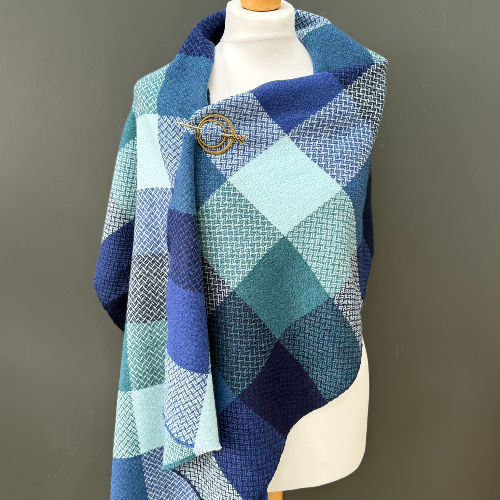 Mannequin wearing a blue, teal, and white plaid scarf against a gray background, with a calm, cozy look.