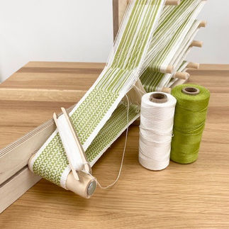 inkle loom with a green and white braid beign woven