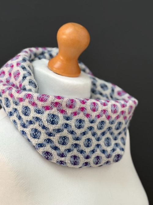 Thumbnail: pink, pale blue and white handwoven snood scarf on  a mannequin against a dark grey wall