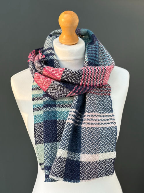 handwoven randomly patterned blue and pink scarf on a mannequin against a dark grey wall