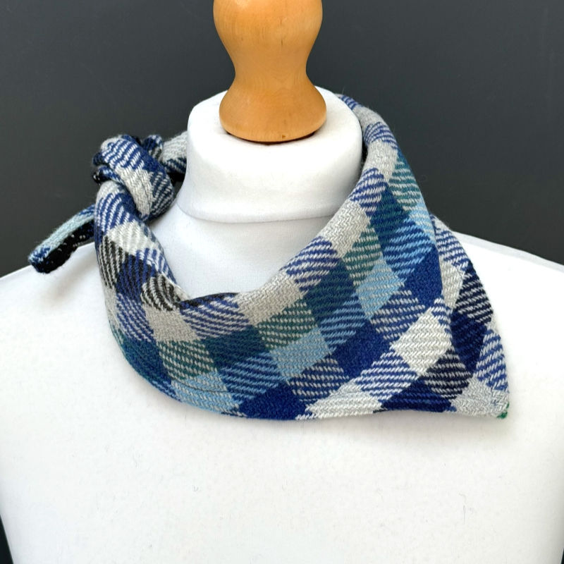 White mannequin wearing a blue, gray, and teal plaid neck scarf against a dark background