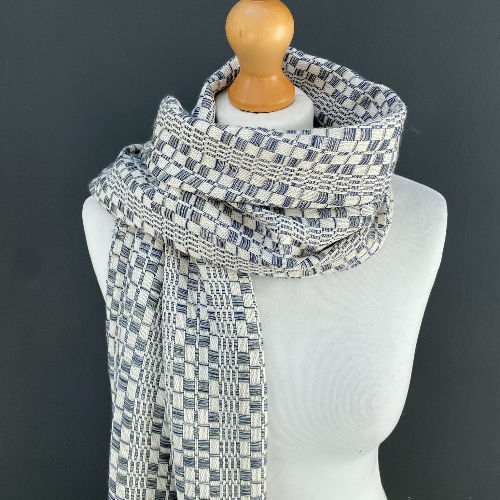 Mannequin wearing a patterned blue and white scarf, wrapped elegantly. Dark grey background enhances the textile's intricate design.