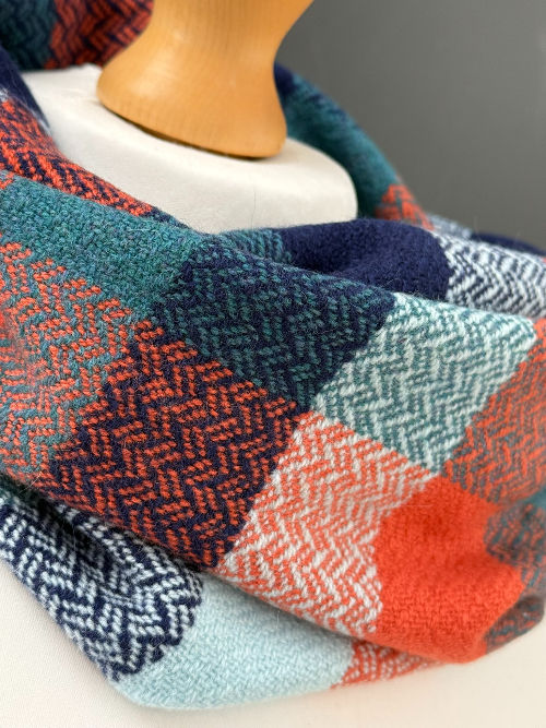 Thumbnail: close up of an emma baker handwoven navy blue, orange and turquoise snood scarf