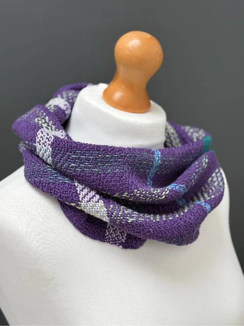 purple woven snood scart with accents of green, teal and lilac on a mannequin around the neck