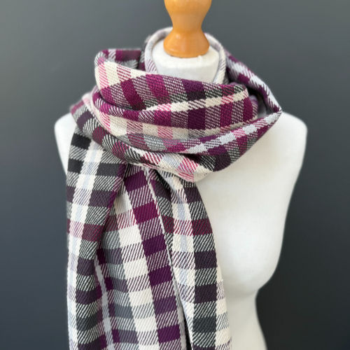 Checkered scarf in red, purple, and gray draped on a mannequin against a dark gray background. No text visible.