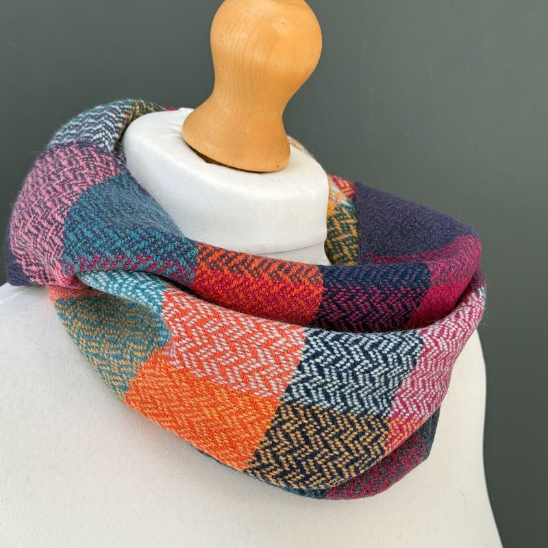 Colorful patchwork knit scarf draped around a white mannequin bust against a gray background.
