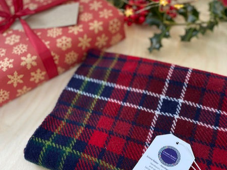 Plaid fabric with a tag next to a red gift box with snowflake pattern. Holly and soft lights in background suggest a festive mood.