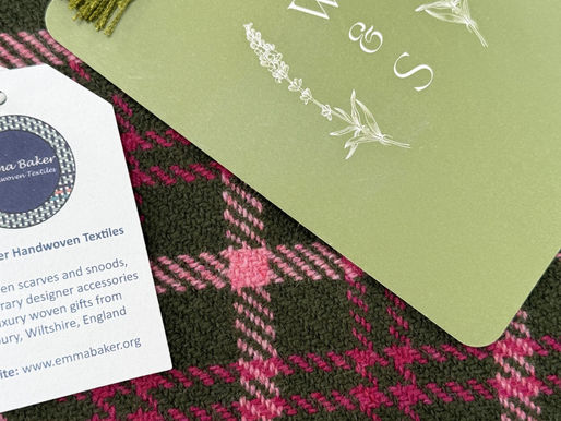 Green card with floral W&S monogram beside an Emma Baker woven textiles business card on pink-and-olive tartan fabric.