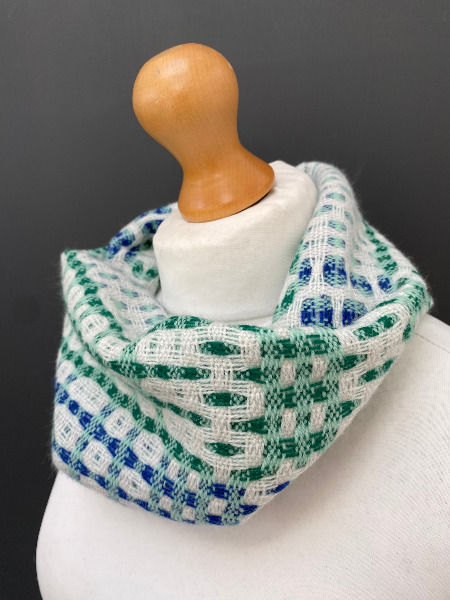 Thumbnail: pale mint green and white intricately patterned snood scarf on a mannequin against a dark grey wall