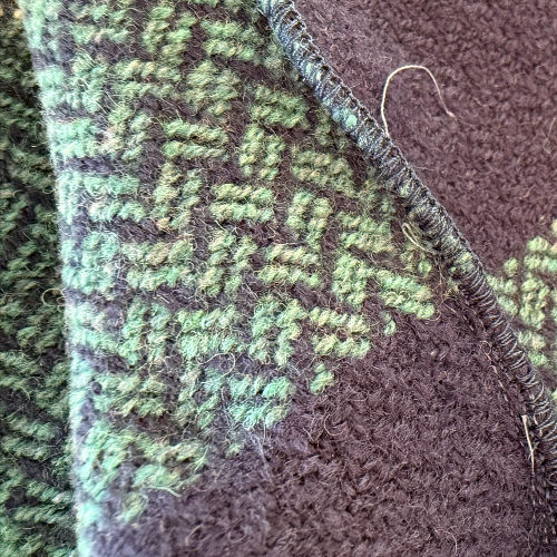Close-up of a green-and-purple woven fabric with a stitched seam and fuzzy texture, filling the frame.