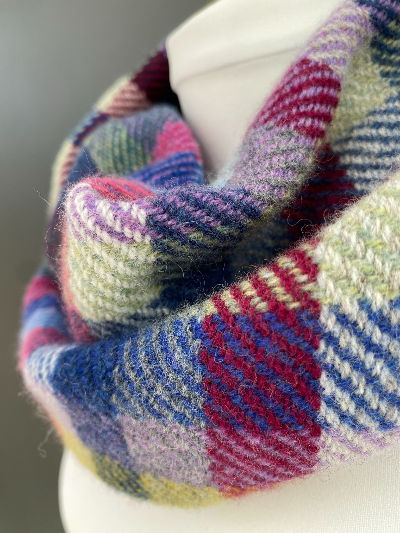 Colorful plaid wool scarf draped on white mannequin. Scarf features red, blue, green, and purple hues, creating a cozy, warm feel.