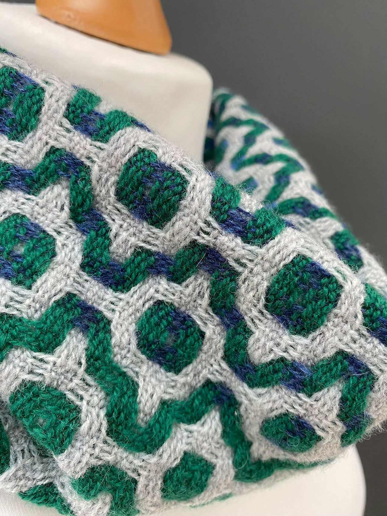 Close u view of a green and light grey mosaic patterned snood scarf