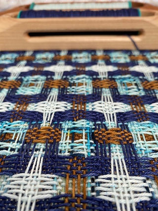 weaving on the floor loom with navy, teal and brass colours of handdyed yarn