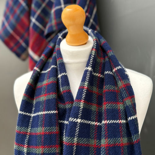 Mannequin draped with blue, red, and white plaid scarf, set against blurred background with matching pattern. Cozy and stylish display.