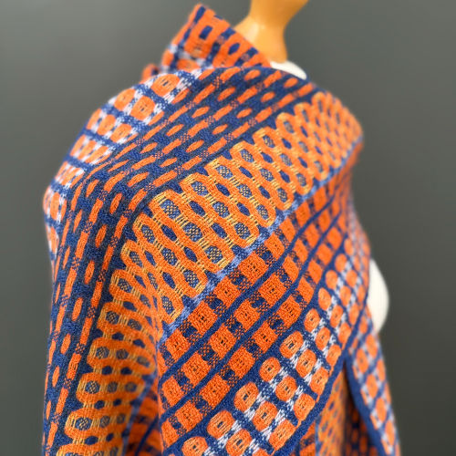 Close-up of a mannequin draped in a blue and orange geometric patterned scarf against a gray background.