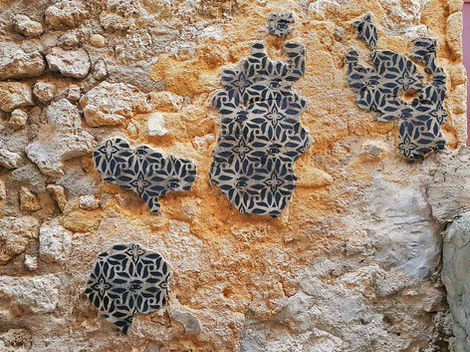 Spraypainted stencil on patches of plaster forming island-like shapes on a cracked historic wall, Favara, Sicily