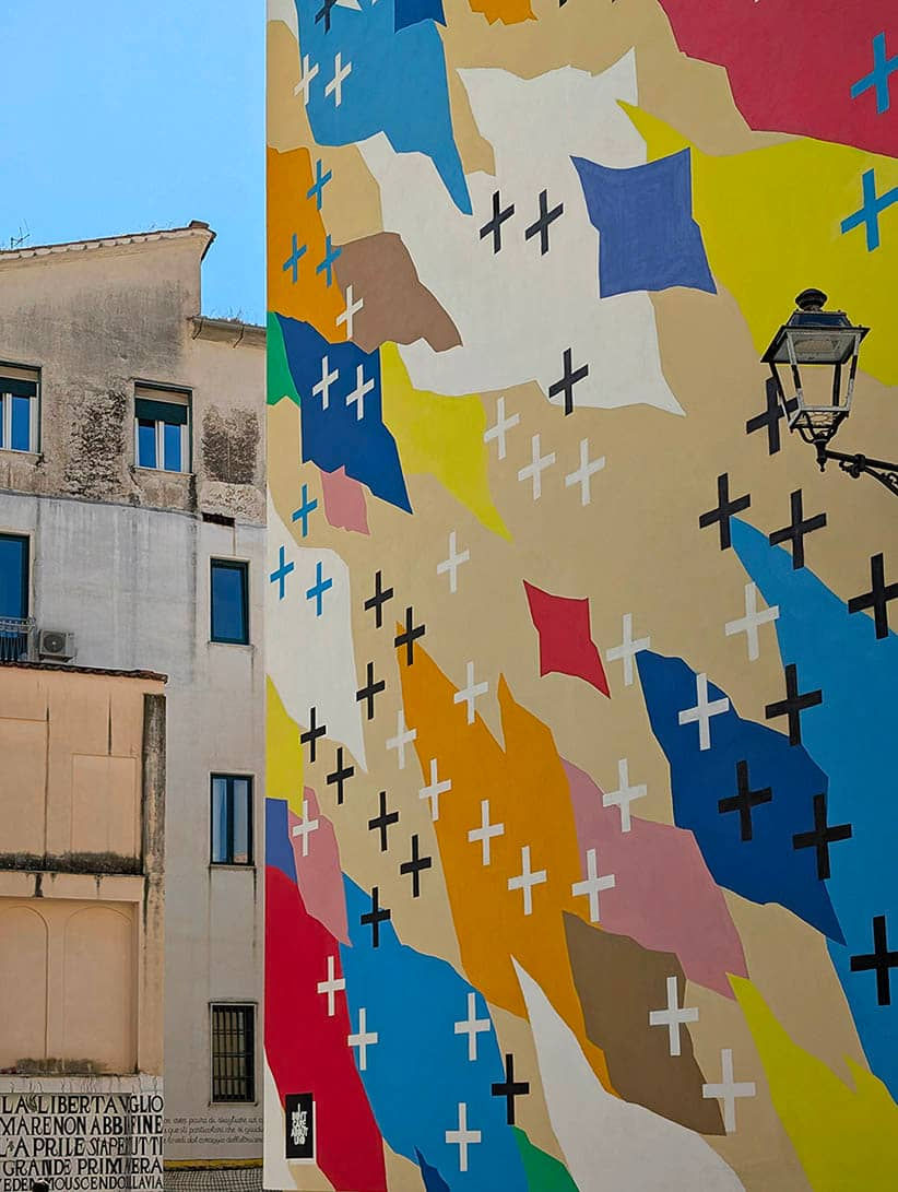 Textures and urban heritage: a detailed shot of UNO's contemporary mural in Salerno, where bold shapes and vibrant color fields meet the aesthetic of a traditional city street lamp.