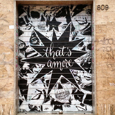 View of the finished "That's Amore" street art on a commercial shutter in Rome, contrasting the artwork with the building's stone façade.