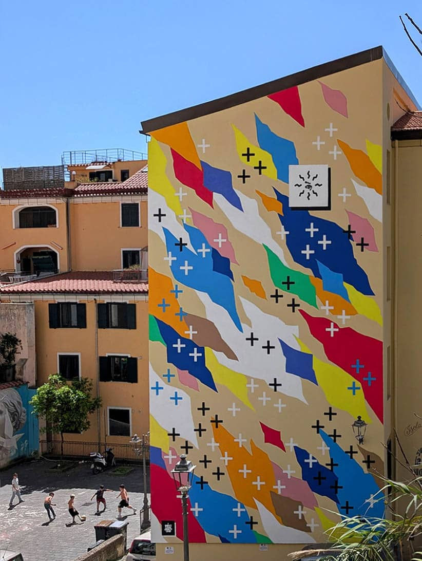 Community and urban art in Salerno: UNO's mural 'To See The Stars Again' towers over the Fornelle district, as local children play football in the square.