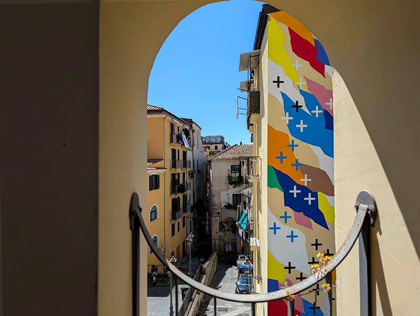 UNO mural Salerno: contemporary urban art viewed through a traditional stone archway.
