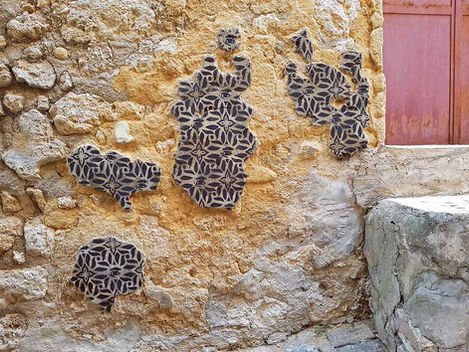 Spraypainted stencil on patches of plaster forming island-like shapes on a cracked historic wall, Favara, Sicily