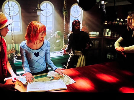 Nami in glasses, next to Luffy, stands over a map and looks at  Sanji, who demonstrates something as Usop takes a step back, and Zoro lays on a sofa, looking out of the widow with his swords