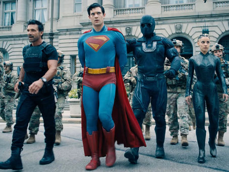 From Left to Right, Rick Flag Sr. and Superman in cuffs, walks with his hands behind his back. Ultra Man is behind him with a hand on his back. The Engineer walks next to Ultra Man. They all are flanked by U.S Military soldiers.