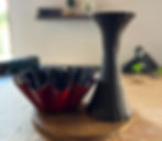 Red and black fluted vase and bowl on a wooden surface. Blurry background with shelves and soft lighting. Calm, artistic setting.