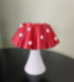 Red and white toadstool-shaped item with polka dots on a black table, set against a neutral wall.