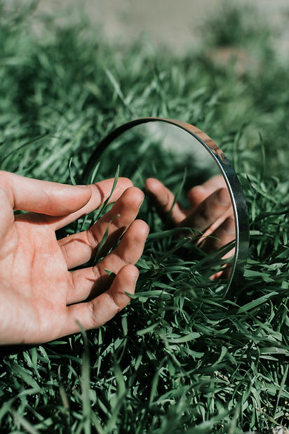 Main tenant tenant's hand touches grass near mirror, reflecting nature, close-up
