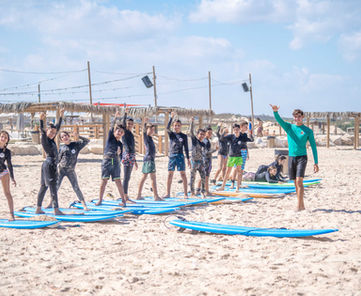 ילדים עומדים על גלשנים בחוף הים במהלך מחנה גלישה לילדים
