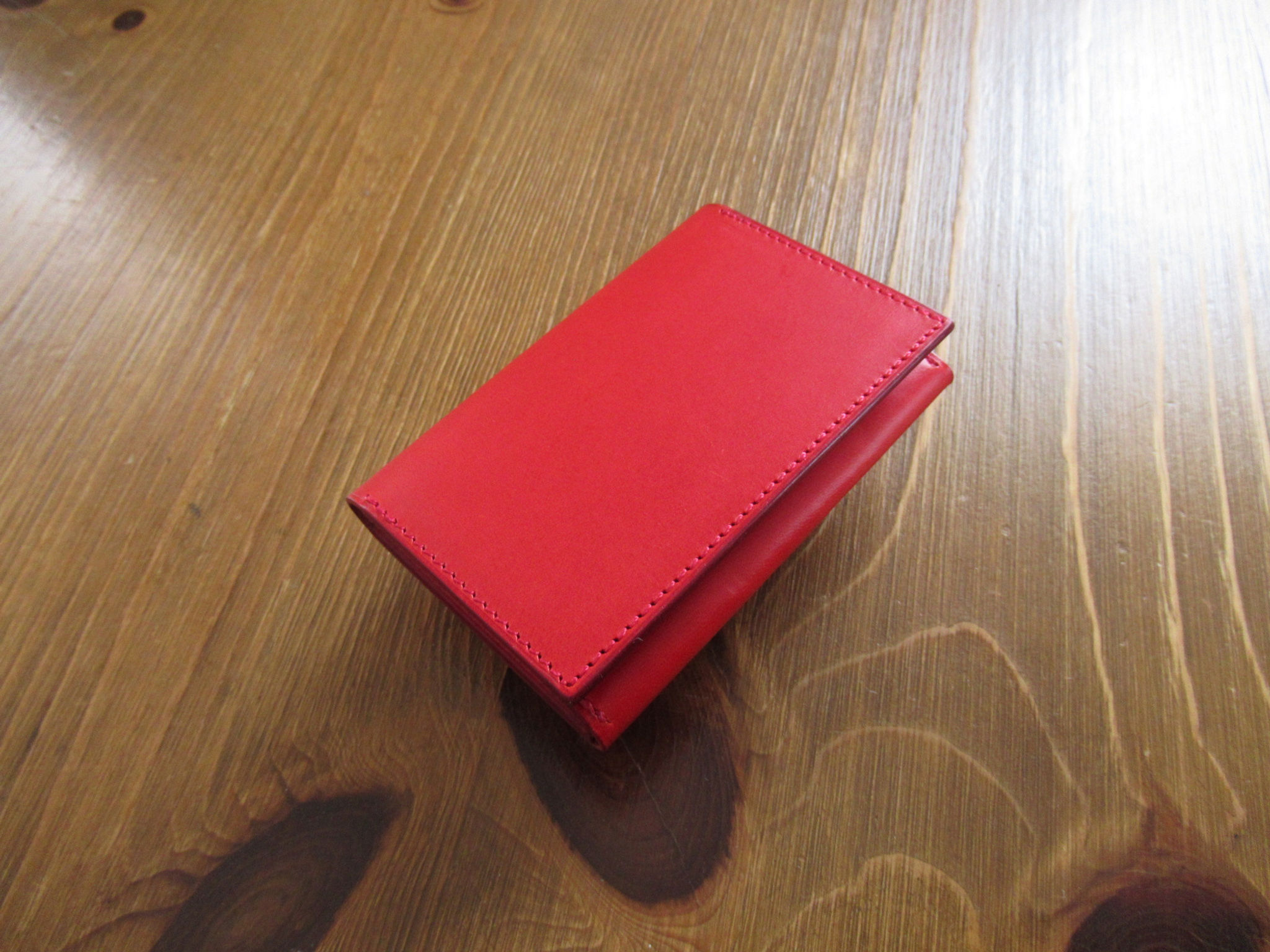 ブッテーロレザー使用の横型カードケースの赤を卓上に置いて
