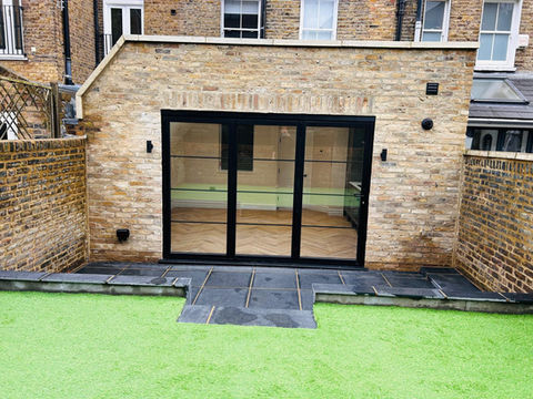 Exterior view of a modern building with glass doors and a green lawn.