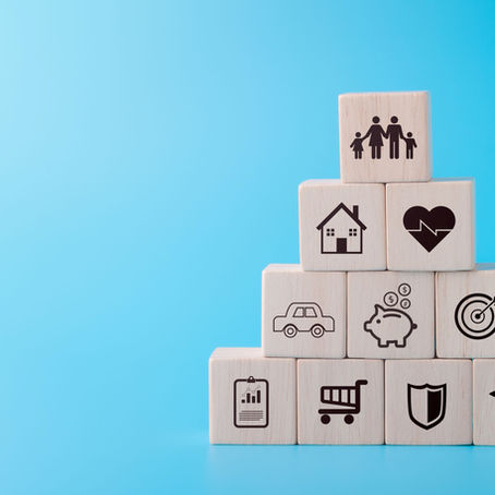 A set of colorful building blocks labeled with various monthly expenses such as car, home, family, and groceries, illustrating the importance of taking out life insurance when buying your first home to protect your financial future.
