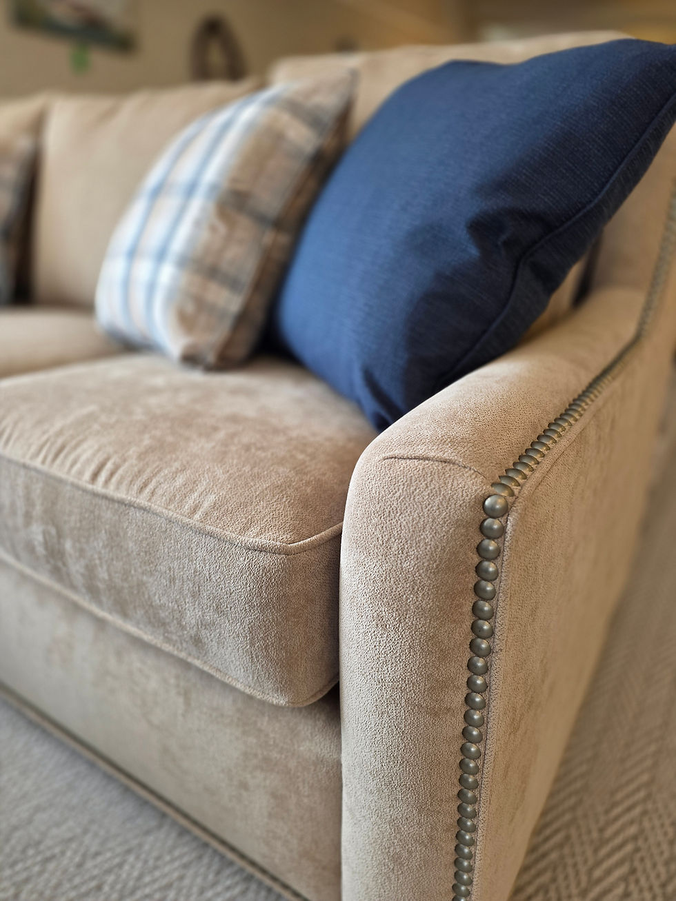 A close-up view of a premium upholstered sofa at Werner Harmsen, highlighting the tight, even stitching, decorative brass nailhead trim, and the rich texture of the high-quality fabric.